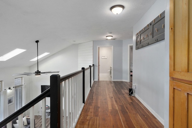 hall with dark wood-style floors, baseboards, lofted ceiling with skylight, and an upstairs landing