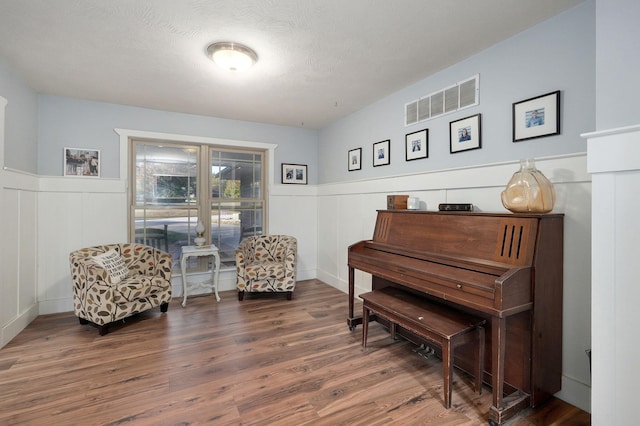 sitting room featuring a textured ceiling, visible vents, dark wood-style flooring, and wainscoting