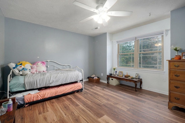 bedroom with ceiling fan, wood finished floors, visible vents, and baseboards