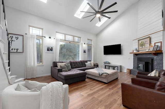 living room with a skylight, baseboards, wood finished floors, stairs, and high vaulted ceiling