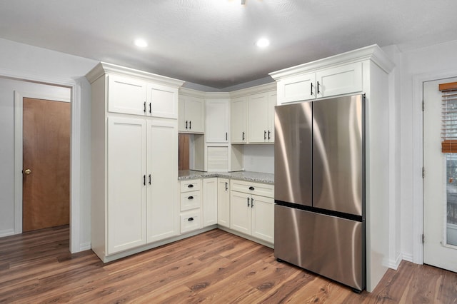 kitchen featuring light stone counters, dark wood-style flooring, freestanding refrigerator, and white cabinetry