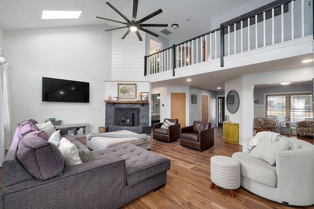 living area featuring a skylight, visible vents, a stone fireplace, wood finished floors, and high vaulted ceiling