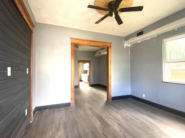 spare room with ceiling fan, wooden walls, a textured ceiling, wood finished floors, and baseboards