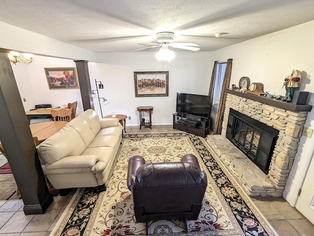 living room with decorative columns, a ceiling fan, a textured ceiling, and a stone fireplace