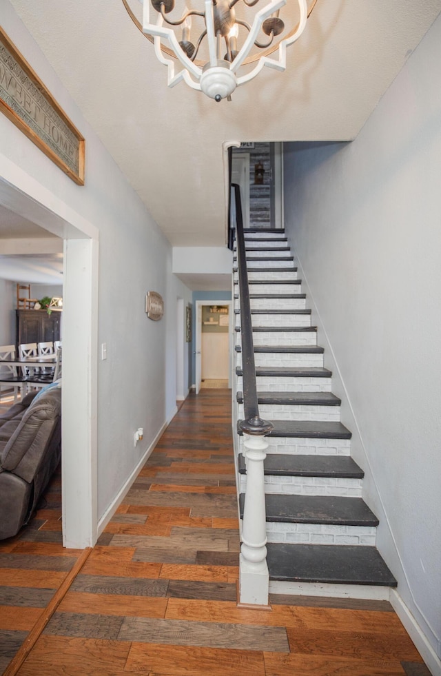 stairs with a chandelier, wood finished floors, and baseboards