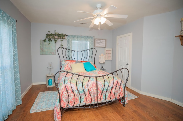 bedroom with ceiling fan, wood finished floors, visible vents, and baseboards