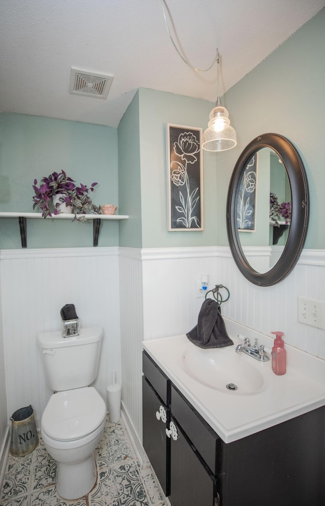 half bath featuring a wainscoted wall, visible vents, toilet, vanity, and tile patterned floors