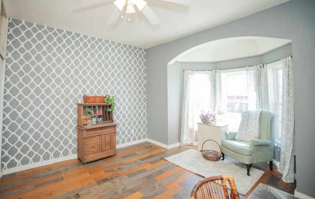 sitting room with wallpapered walls, baseboards, arched walkways, an accent wall, and wood finished floors