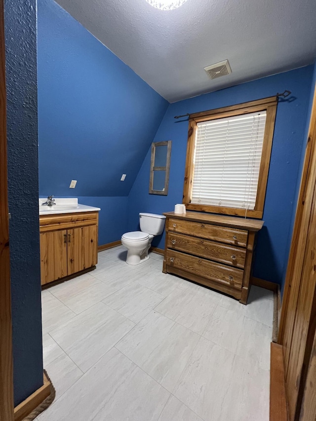 bathroom with a textured ceiling, lofted ceiling, toilet, vanity, and visible vents