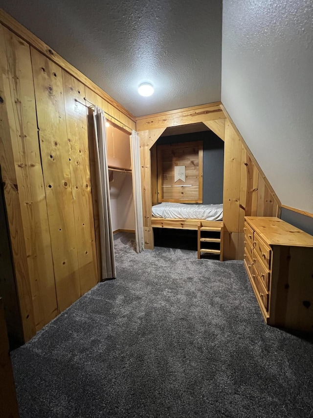 unfurnished bedroom with carpet flooring, vaulted ceiling, wooden walls, and a textured ceiling