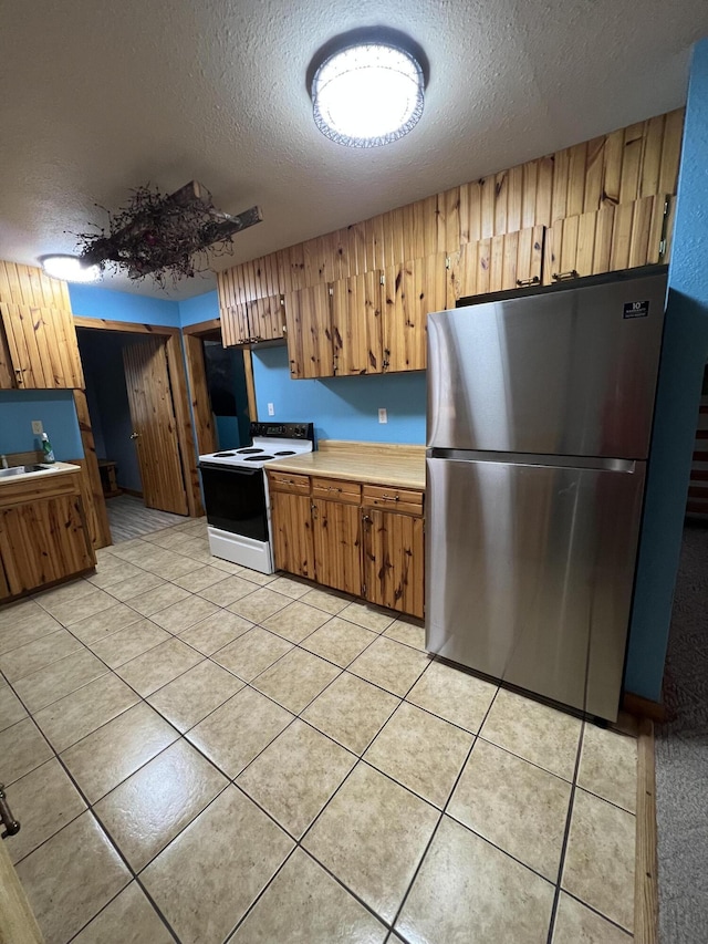 kitchen with light countertops, electric range, brown cabinetry, and freestanding refrigerator