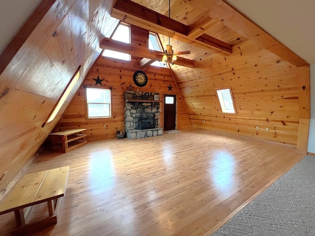 living room with wood walls, lofted ceiling with skylight, wood finished floors, and a stone fireplace