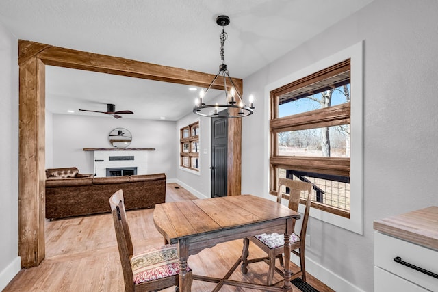 dining space with baseboards, beamed ceiling, a fireplace, and light wood-style floors