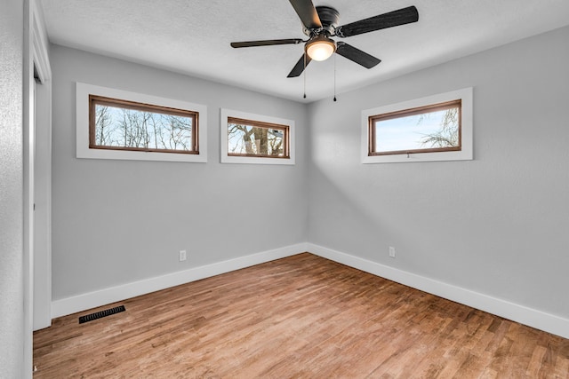 empty room with baseboards, wood finished floors, visible vents, and a healthy amount of sunlight