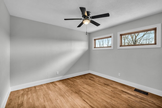 unfurnished room featuring baseboards, visible vents, ceiling fan, and wood finished floors