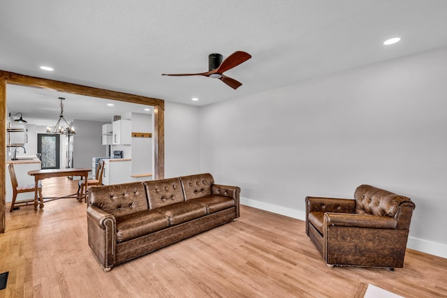 living area with baseboards, recessed lighting, ceiling fan with notable chandelier, and light wood-style floors