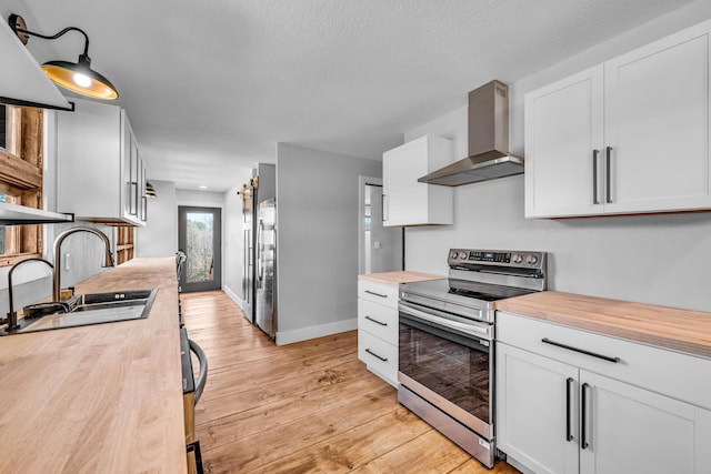 kitchen with wall chimney exhaust hood, stainless steel appliances, white cabinetry, wooden counters, and a sink