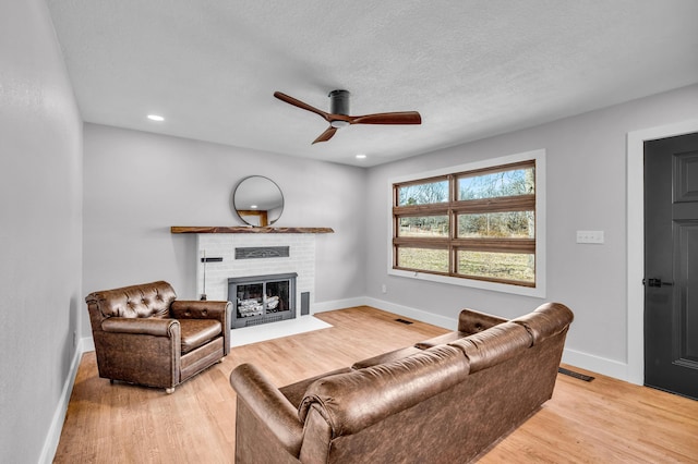 living area featuring visible vents, a brick fireplace, light wood-style flooring, and baseboards