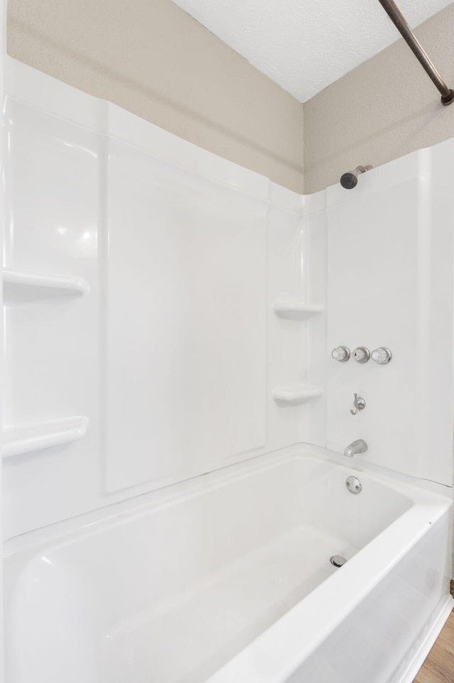 bathroom featuring a textured ceiling, wood finished floors, and washtub / shower combination