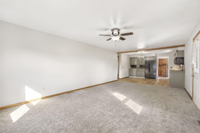 unfurnished living room with carpet floors, baseboards, and ceiling fan with notable chandelier