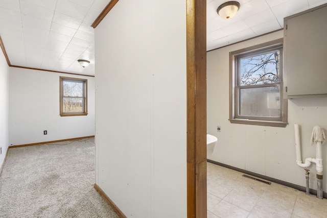 hallway featuring baseboards, ornamental molding, visible vents, and light colored carpet