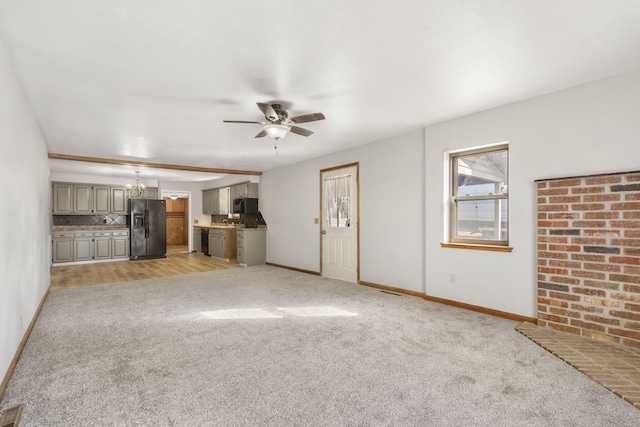 unfurnished living room featuring light carpet, baseboards, and ceiling fan with notable chandelier