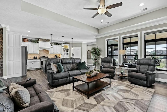 living room with ceiling fan, wood finished floors, visible vents, baseboards, and crown molding