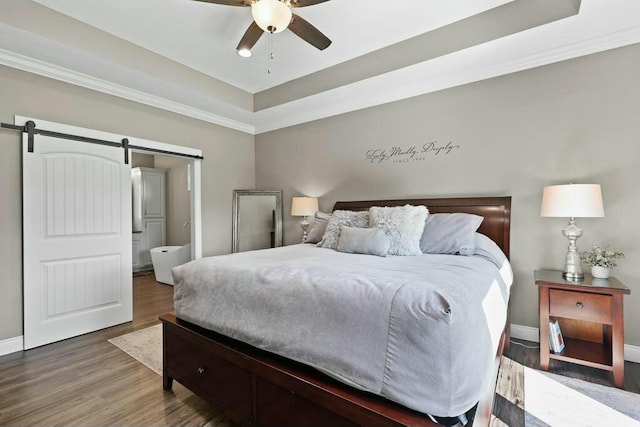 bedroom with a tray ceiling, wood finished floors, baseboards, and a barn door