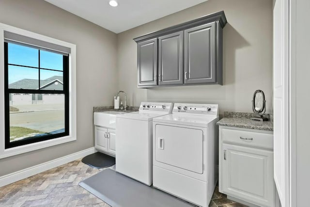 laundry room with cabinet space, baseboards, brick floor, washer and dryer, and a sink