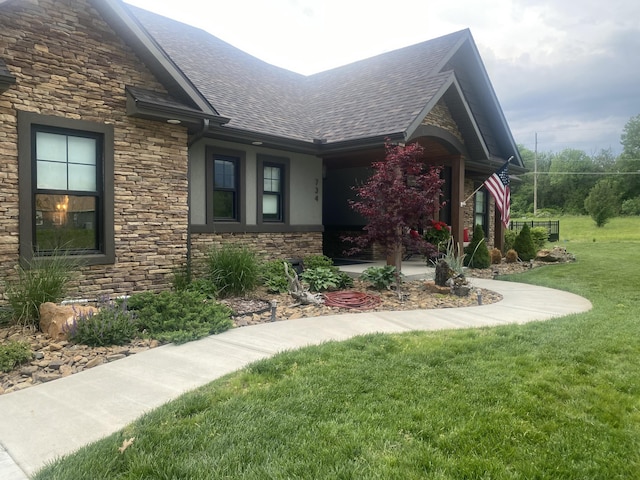 exterior space featuring stone siding, stucco siding, a lawn, and roof with shingles