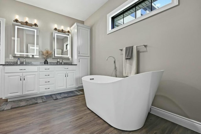 bathroom with a sink, double vanity, a soaking tub, and wood finished floors