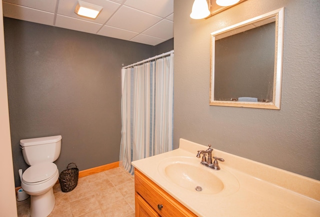 bathroom featuring a paneled ceiling, toilet, vanity, baseboards, and tile patterned floors