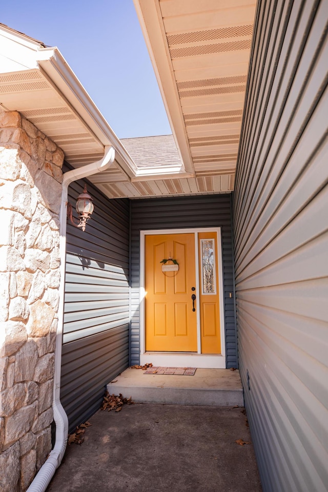 entrance to property featuring stone siding and a shingled roof