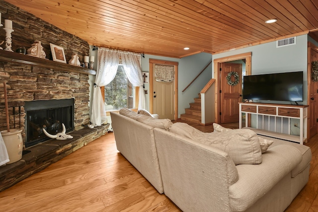 living room with visible vents, wood ceiling, stairway, wood finished floors, and a stone fireplace