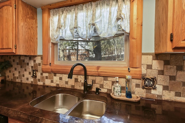 kitchen with backsplash, dark countertops, a sink, and brown cabinets