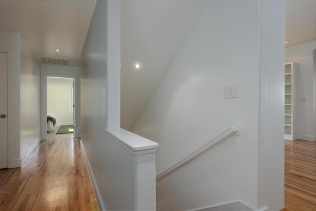 hall with visible vents, wood finished floors, an upstairs landing, and baseboards