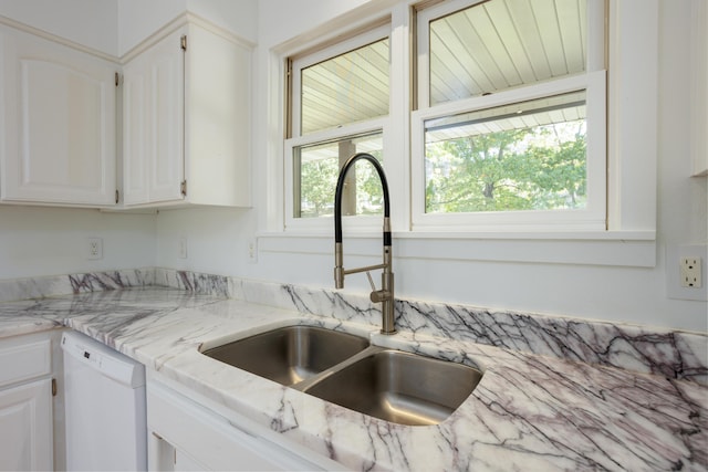 kitchen with light stone counters, white cabinets, white dishwasher, and a sink