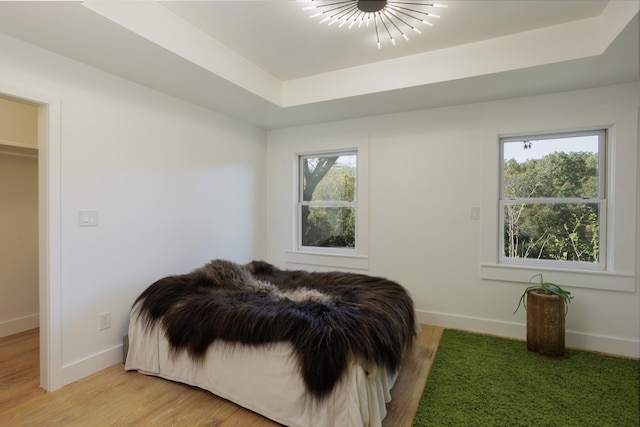 bedroom featuring multiple windows, a raised ceiling, light wood-style flooring, and baseboards