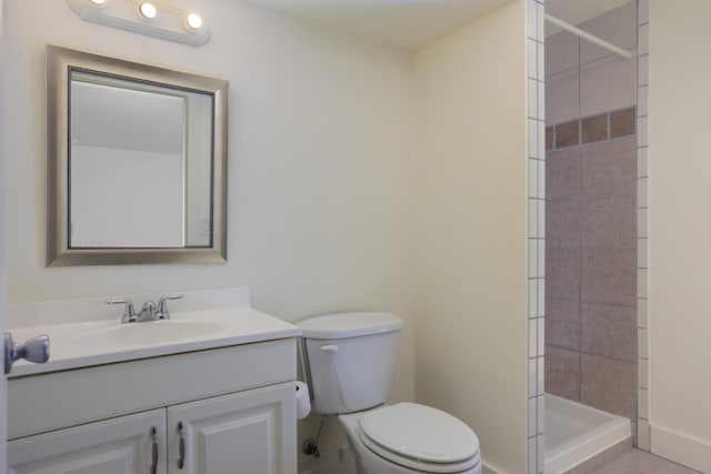 bathroom with toilet, baseboards, tiled shower, and vanity