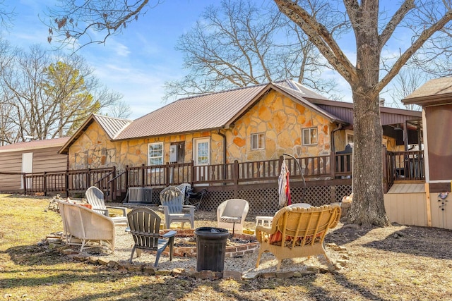 back of house featuring stone siding, a fire pit, metal roof, and a wooden deck