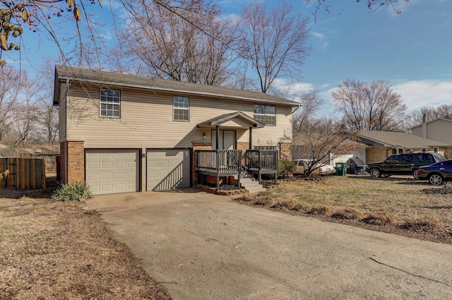 raised ranch featuring a garage, concrete driveway, brick siding, and fence