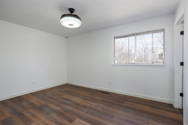 empty room with visible vents, baseboards, dark wood finished floors, and a textured ceiling