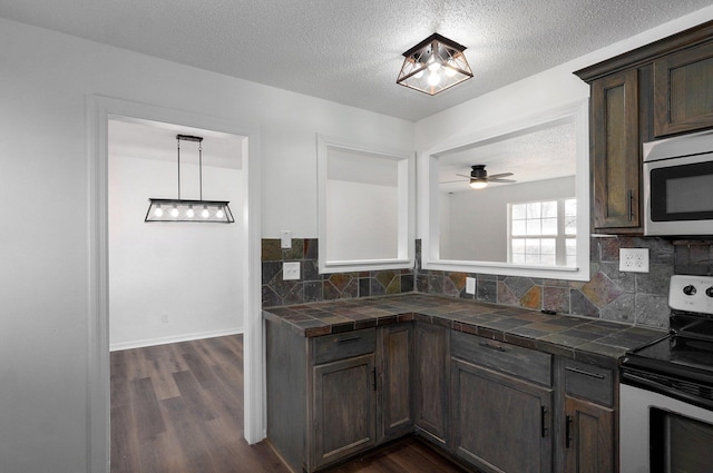 kitchen featuring tile countertops, a textured ceiling, appliances with stainless steel finishes, dark wood-style floors, and tasteful backsplash