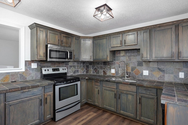 kitchen with tile countertops, stainless steel appliances, decorative backsplash, dark wood-type flooring, and a sink