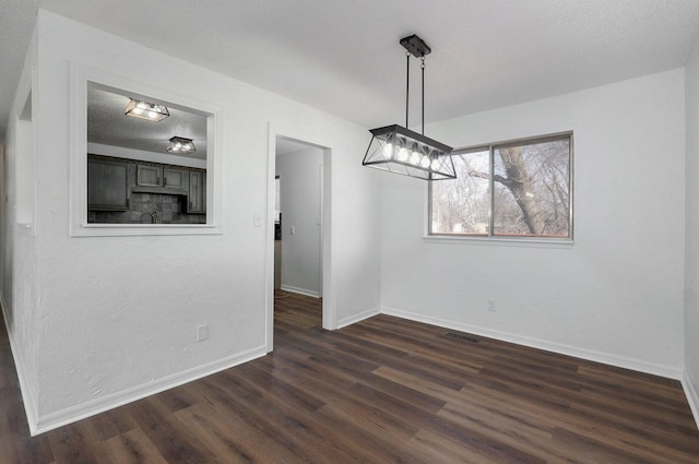 unfurnished dining area with visible vents, dark wood finished floors, a textured ceiling, and baseboards