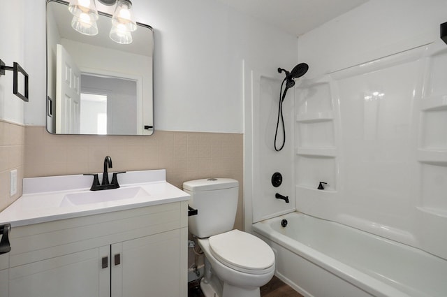 bathroom featuring toilet, a wainscoted wall,  shower combination, vanity, and tile walls