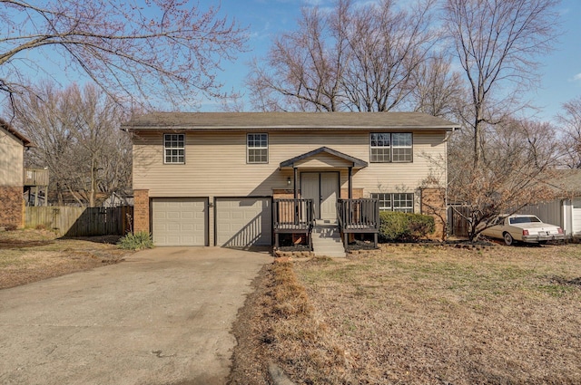 raised ranch featuring driveway, an attached garage, fence, and brick siding