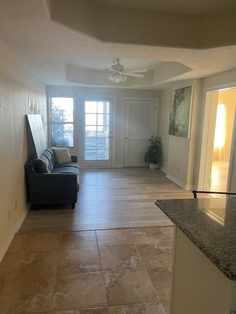 doorway featuring baseboards, a tray ceiling, and ceiling fan