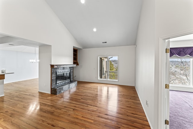 unfurnished living room featuring high vaulted ceiling, a fireplace, wood finished floors, and a healthy amount of sunlight