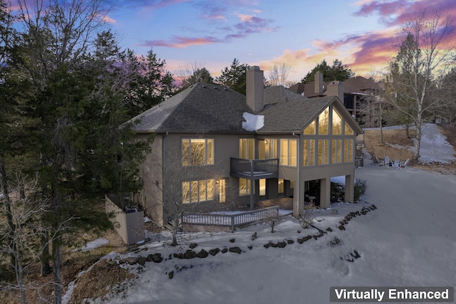 back of property at dusk with a shingled roof, a sunroom, and a chimney